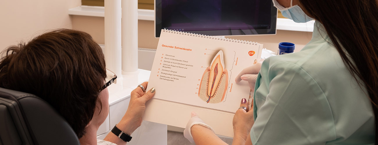 Eine Mitarbeiterin der Praxis Zahnärzte im Schloss in Berlin Steglitz erklärt einer Patientin, wie endodontische Behandlungen wie die Wurzelbehandlung oft Zähne retten.