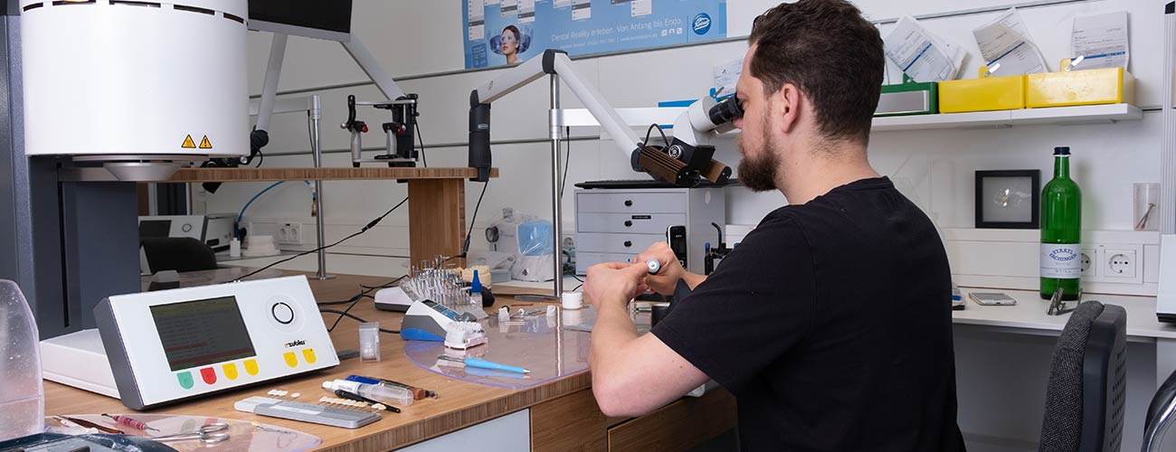 Zahntechnikermeister Chris Vörös schaut durch ein Mikroskop und fertigt ästhetischen und hochwertigen Zahnersatz im Meisterlabor dent-a-pur für die Zahnärzte im Schloss in Berlin Steglitz.